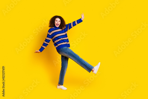 Full length photo of ovejoyed funny girl wear knit pullover jeans danicing on one leg have fun isolated on yellow color background photo
