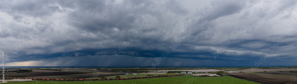 Aerial panoramic view of a large blue-gray colored rain and thunder cloud over a flat prairie setting. A train can be seen on a track along the bottom of the image.
Aerial panoramic view of a large blue-gray colored rain and thunder cloud over a flat prairie setting. A train can be seen on a track along the bottom of the image.