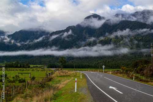 Road through green valley with mountains and clouds