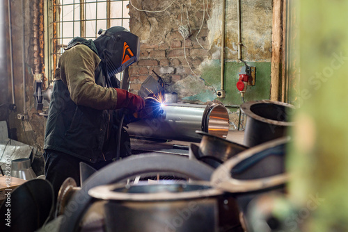 Male welder is welding stainless pipe in industrial workshop photo