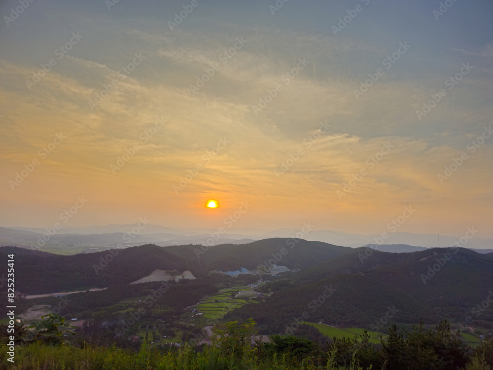 A beautiful sunset over a mountain range with a small town in the valley below. The sky is filled with clouds and the sun is setting, creating a warm and peaceful atmosphere A beautiful sunset over a mountain range with a small town in the valley below. The sky is filled with clouds and the sun is setting, creating a warm and peaceful atmosphere