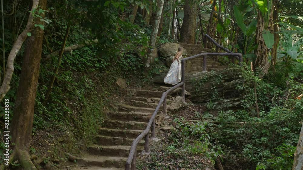 Woman in white dress walking up stone steps surrounded by lush green forest and tropical vegetation. pathway is lined with wooden handrails, and scene evokes sense of exploration and nature. Woman in white dress walking up stone steps surrounded by lush green forest and tropical vegetation. pathway is lined with wooden handrails, and scene evokes sense of exploration and nature.