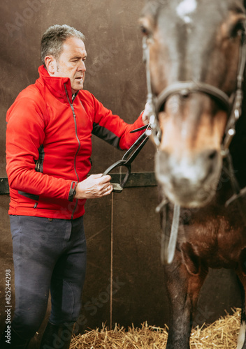 Rider adjusting horse bridle in stable.