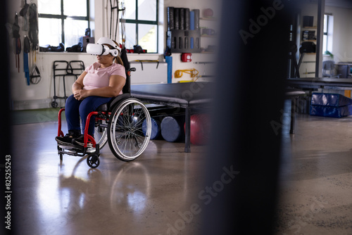 Biracial female paraplegic in wheelchair using VR headset at gym rehab center
