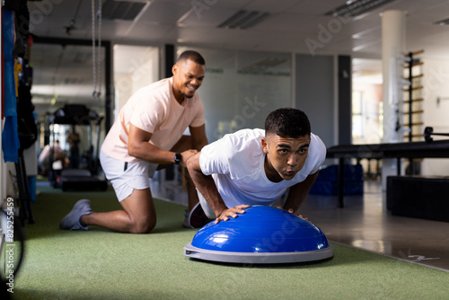 At rehabilitation center, biracial male therapist helping patient with balance dome exercises photo