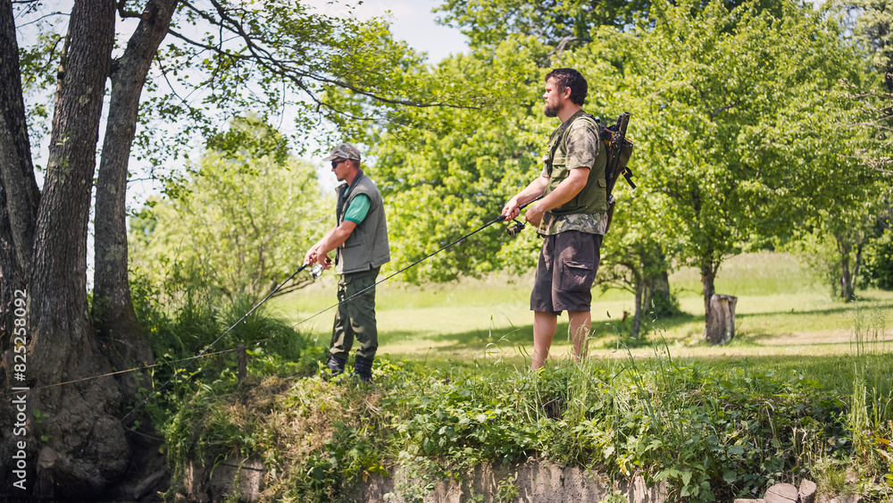 Two fishermen on the river shore, using fishing rods with reels to catch a fish. Concepts of enjoyment and recreation in nature. Two fishermen on the river shore, using fishing rods with reels to catch a fish. Concepts of enjoyment and recreation in nature.