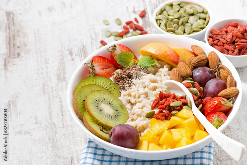 oatmeal porridge with fresh fruits and superfoods and white wooden background