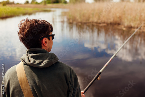 Back view of man fishing wearing military uniform. Guy sitting on bridge across river holding rod. Recreation concept