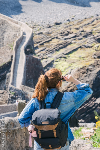 Woman with a backpack standing with a overlook on the stairs at the San Juan Gaztelugatxe, Spain