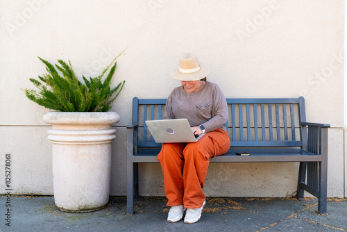 Casual woman sitting with laptop on bench outside photo
