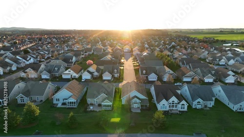 Suburban neighborhood at sunset, with rows of similar houses, green lawns, and a street leading directly into the glowing sun on the horizon. Aerial truck shot. photo
