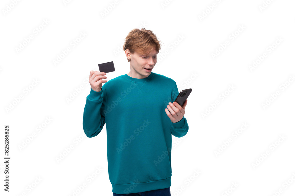 young handsome man with red hair dressed in a blue jacket holds a credit card and a phone young handsome man with red hair dressed in a blue jacket holds a credit card and a phone