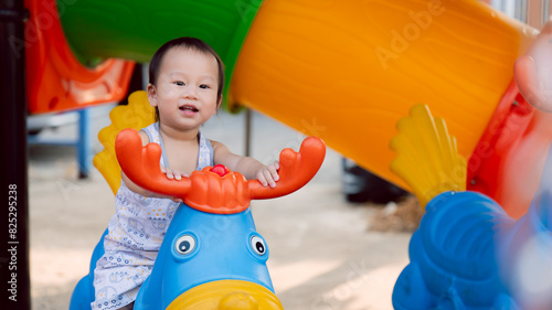 A happy child playing on a colorful playground. Asian boy smiles happily while playing on a spring swinging horse in an outdoor area. In summer or spring time. Emotional and mental development. © Kanthita