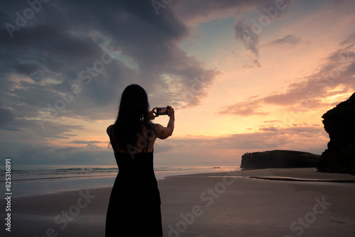 Woman taking pictures of beautiful beach at sunset photo