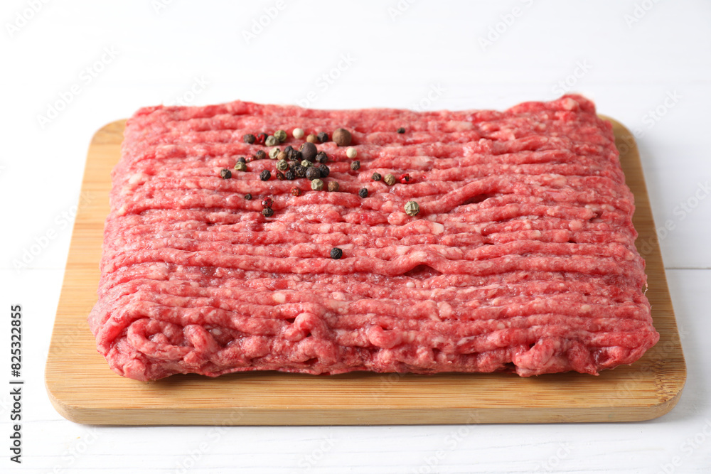 Raw ground meat and peppercorns on white wooden table