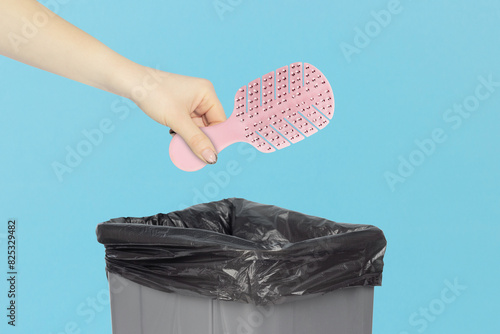 throw the women's hair comb into the trash, outstretched hand with hair comb in front of the trash can, plastic recycling concept