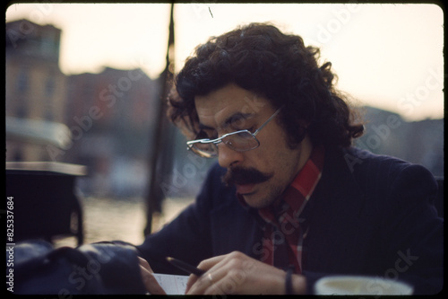 Old 70's film portrait of man writing in outdoor cafe  photo