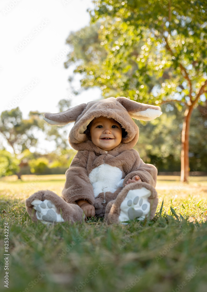 A little girl with a bunny onesie in a park siting down A little girl with a bunny onesie in a park siting down