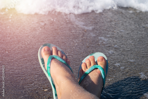 Blue colored summer shoe sandals female woman barefoot on sea shore beach as vacation tourism and holiday concept in front of ocean sea foam background.