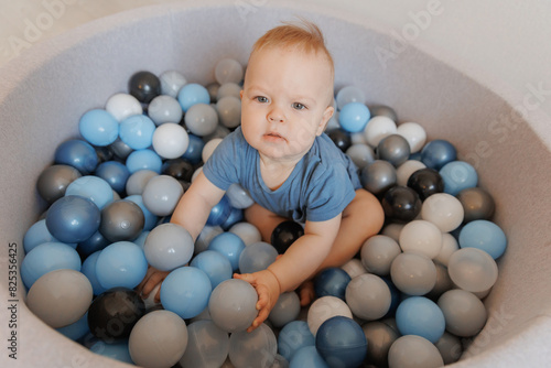 Happy little boy play in dry pool with colorful balls in living room. Concept lifestyle childhood moment photo