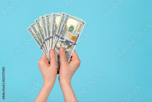 Female hand holding one hundred-dollar bills on blue background. photo
