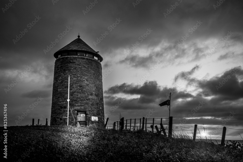 Black and white photo of an old windmill tower by the sea at night Black and white photo of an old windmill tower by the sea at night