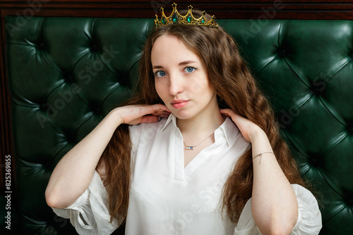 Young woman wearing a crown sitting on a leather sofa