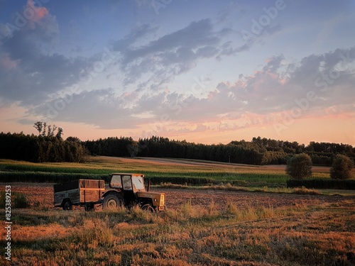 Traktor na tle pola, zachód słońca, niebo z chmurami 