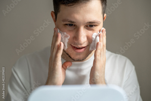 Young man putting cosmetics on his face in front of mirror photo