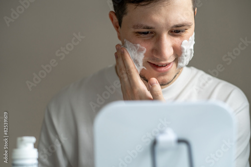 Man applying cleaning or shaving foam on his face in front of mirror photo