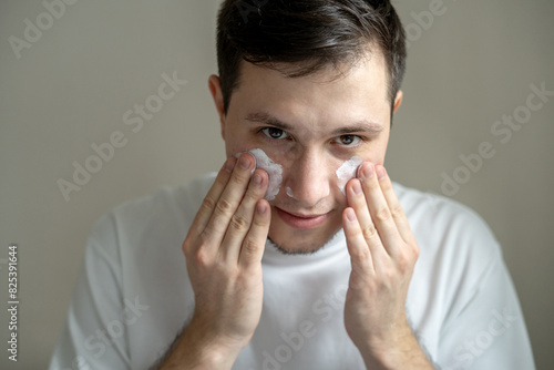 Young man in white t-shirt putting cream on his face photo