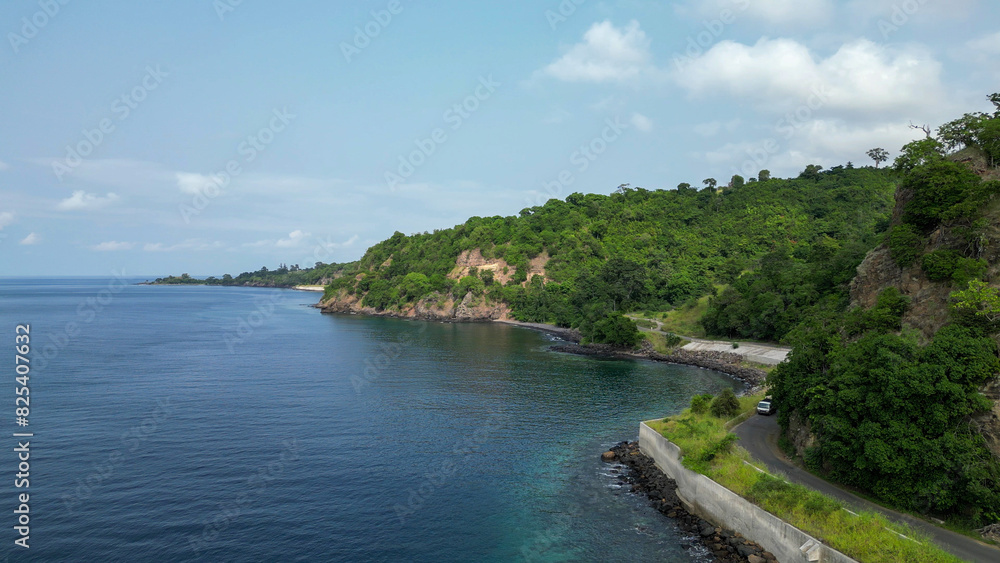 Car drives along the north coastal road between cliffs and the sea in Sao Tome and Principe, Africa