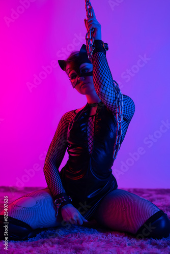 Sexy girl in latex dress bdsm mistress and cat mask in neon light with chains for sex game