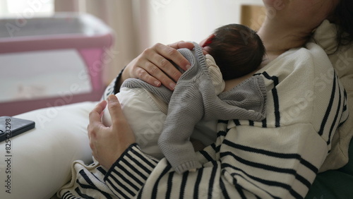 Mother holding newborn baby on chest while taking a nap, woman laid in bed holding infant tight on chest during initial week of life, maternal care affectionate lifestyle scene photo