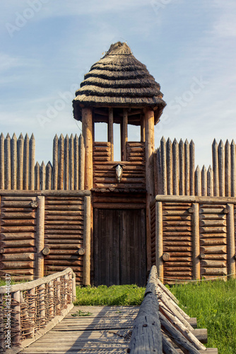 Wooden gate with a tower of an ancient settlement. A gate with a tower at a palisade protecting an ancient settlement, Palisades, a wooden bridge, a tower