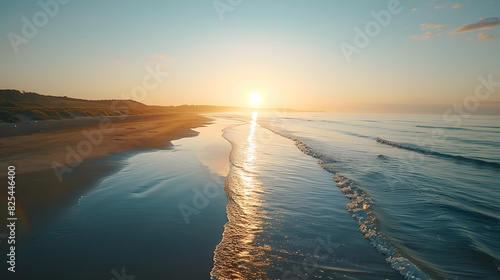 A photo featuring a tranquil sunrise over a deserted beach. Highlighting the first light of day and the calm, reflective waters, while surrounded by long shadows and the soft sound of waves photo