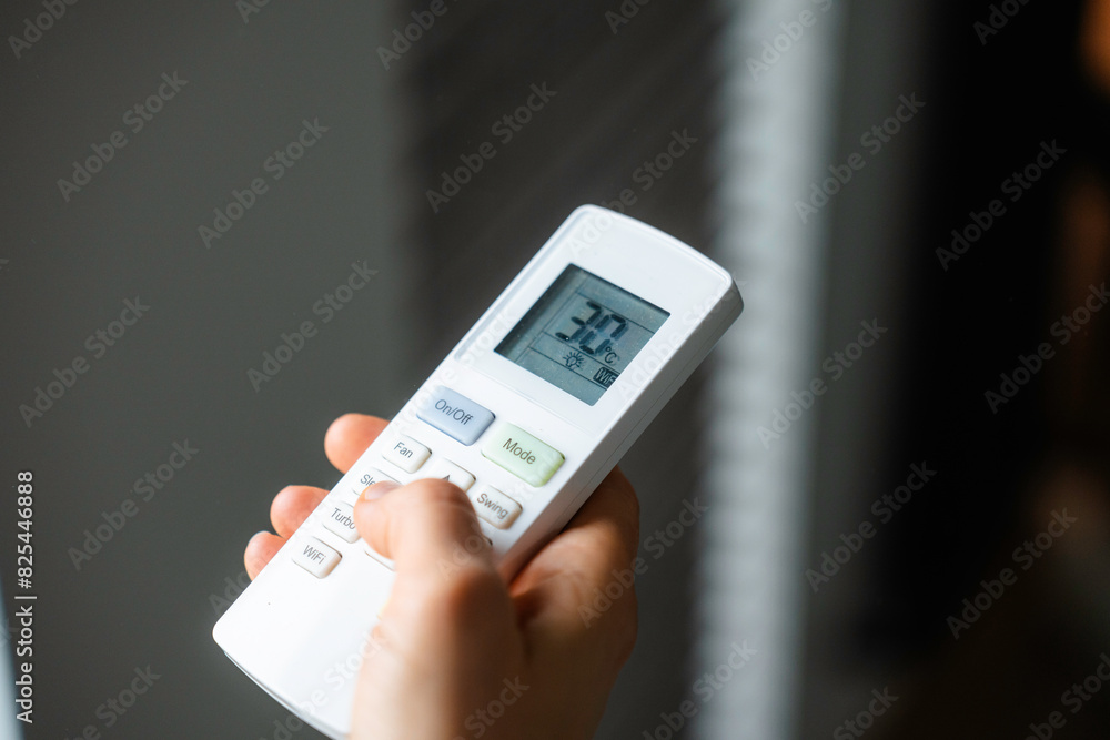The woman controls the air conditioner using the remote control The woman controls the air conditioner using the remote control