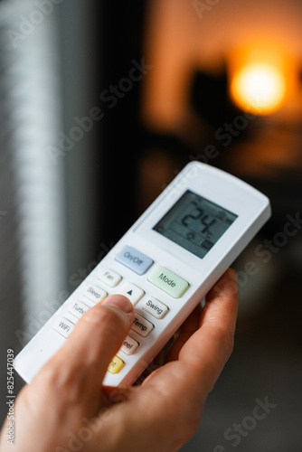 The woman controls the air conditioner using the remote control