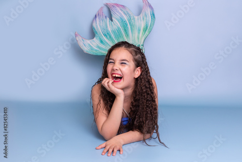 A very happy child girl in a mermaid costume lie isolated on light-blue background