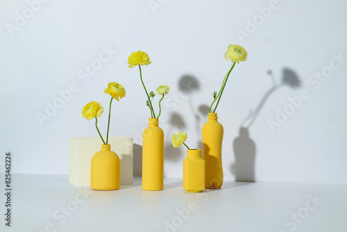 Different glass vases and buttercup flowers on white background photo