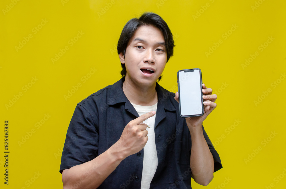 mock up young Asian man showing and pointing at blank screen smartphone. asian man in beige tshirt holding and showing phone screen with happy euphoric shocked wow expression. mock up young Asian man showing and pointing at blank screen smartphone. asian man in beige tshirt holding and showing phone screen with happy euphoric shocked wow expression.