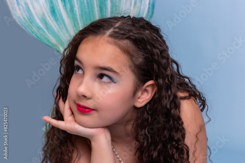 Close up of cute girl in a mermaid costume lie on light-blue background