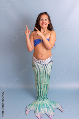 A beautiful child girl in a mermaid costume stand on a blue background