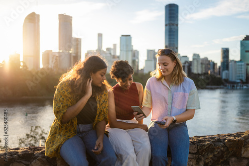 Three young women using smartphone outdoors photo