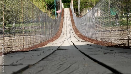 Rope bridge with safety metal fence and wooden planks floor, hanging over the river. photo