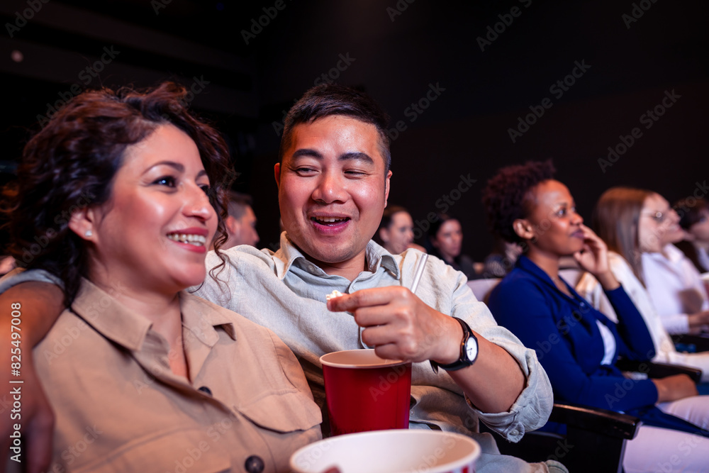 Multiracial Asian and Hispanic couple watching a movie in cinema and eating popcorn.