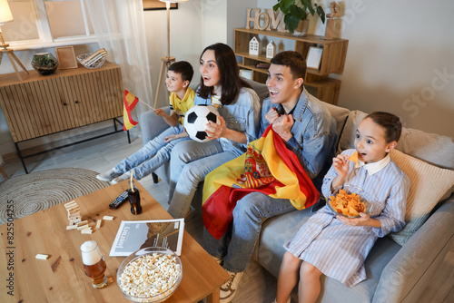 Happy family with Spanish flags watching football game on sofa at home in evening