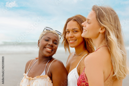 group portrait of three girls with different skin tones and dressed in summer clothes on the beach.