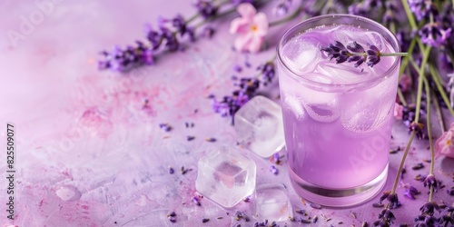 Glass of lavender lemonade with ice and flowers on a pastel pink and lavender background