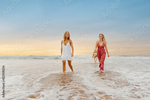 group of female friends in summer dresses walking along the seashore on a summer day at the beach